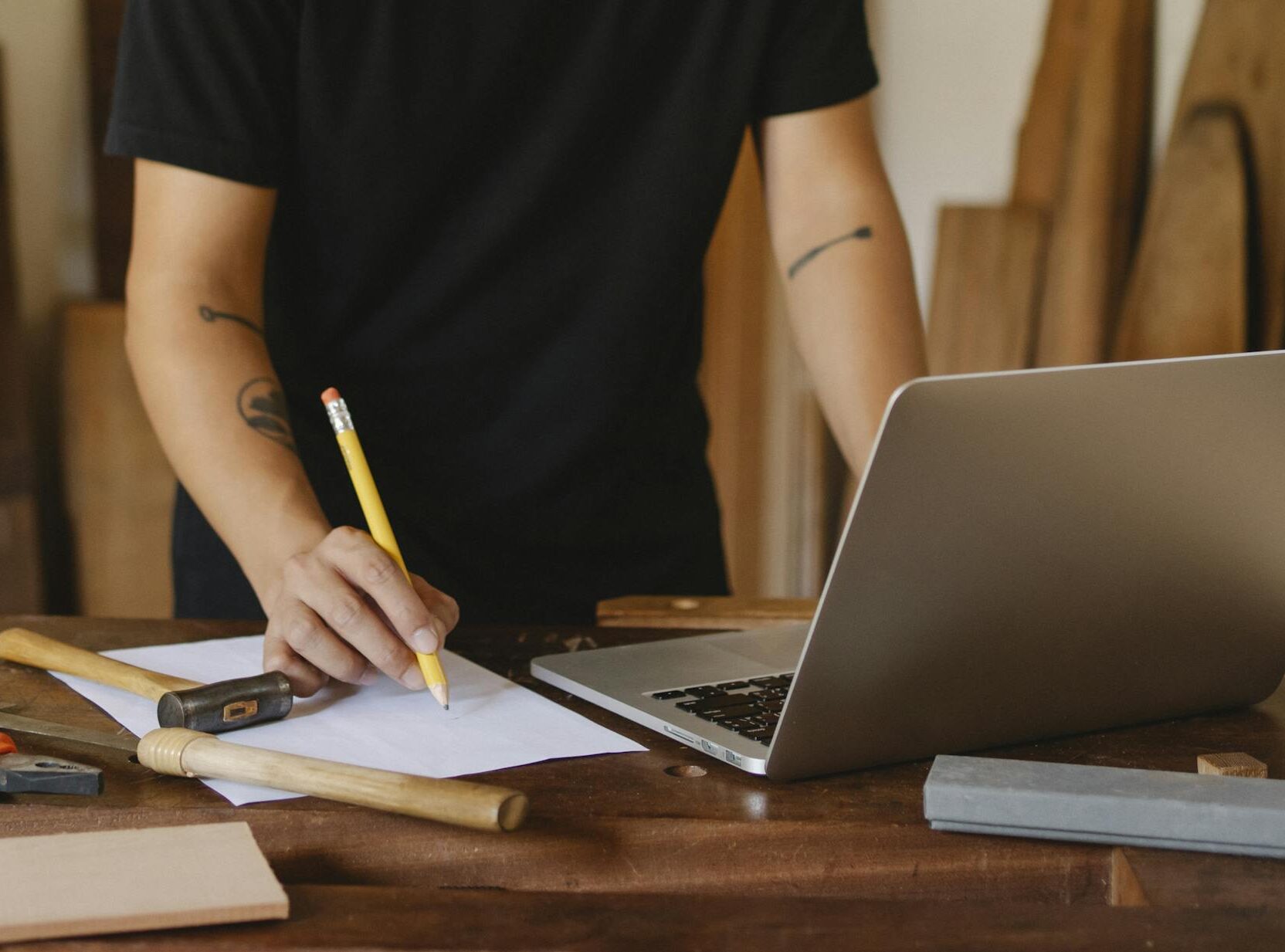 A craftsman planning projects on a laptop amidst tools in a woodwork studio.
